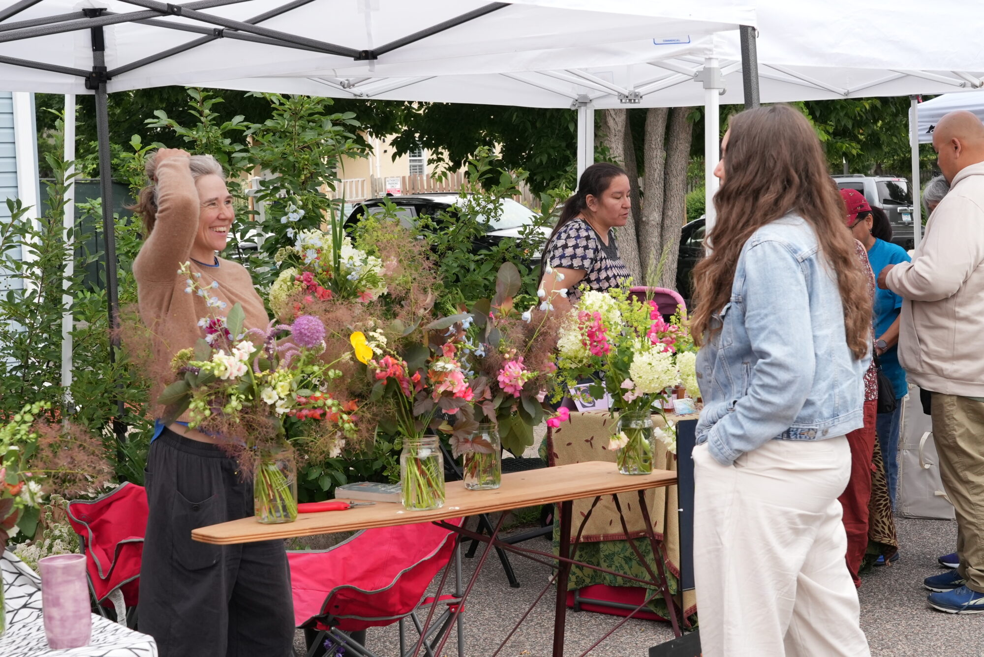 A woman selling flowers chats and smiles at a customer. Other vendors chat in the background